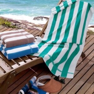 Toalhas de praia listradas personalizadas nas cores bege, azul e verde sobre espreguicadeira